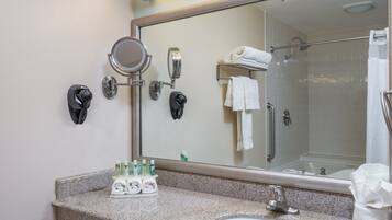 A bathroom with a granite countertop, a sink, a mirror, a towel rack, and a shower area.