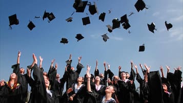 A group of graduates in black gowns and caps, with some caps in mid-air, suggesting a graduation ceremony.