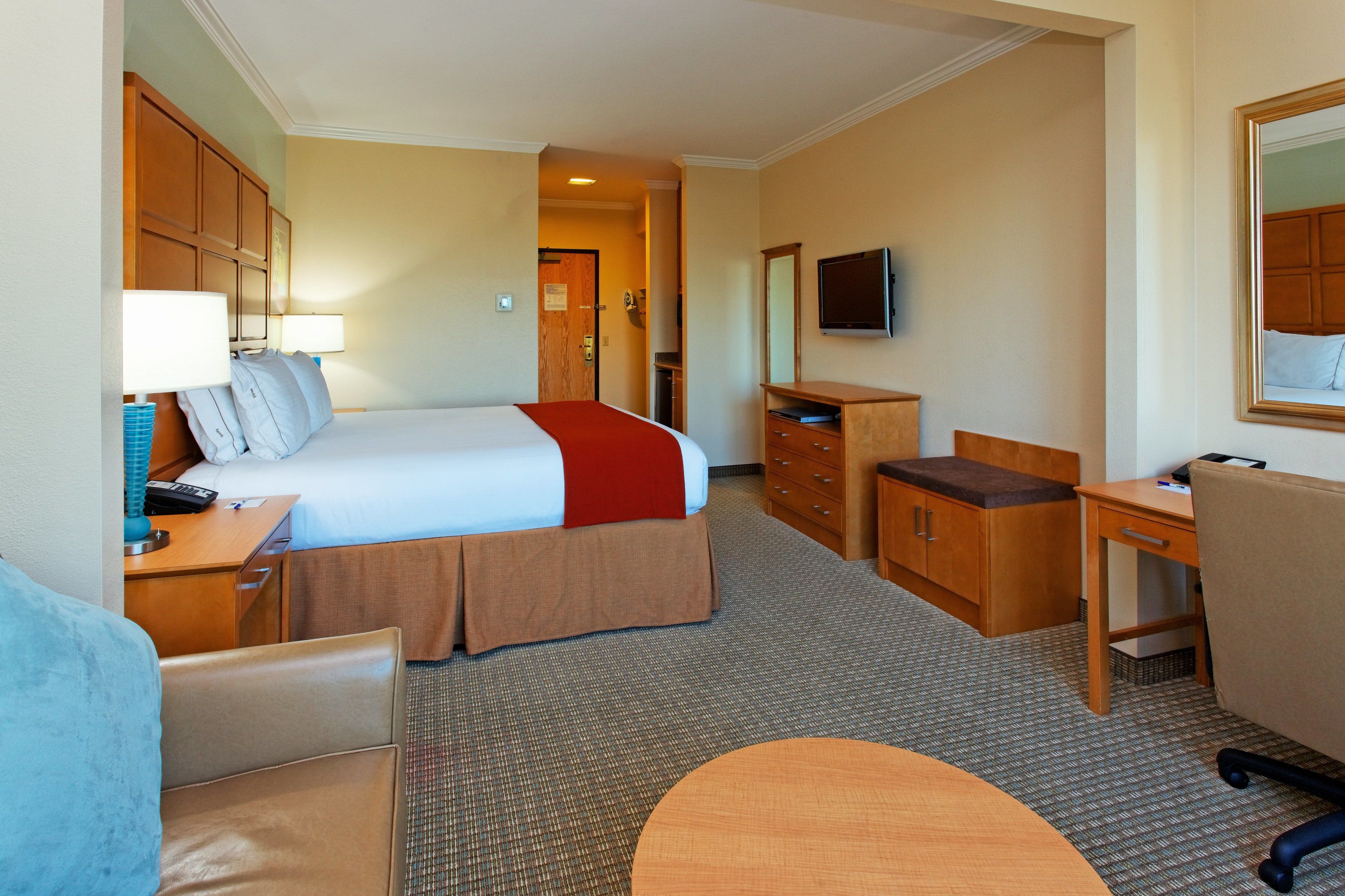 A hotel room with a bed, desk, chair, dresser, and a television.