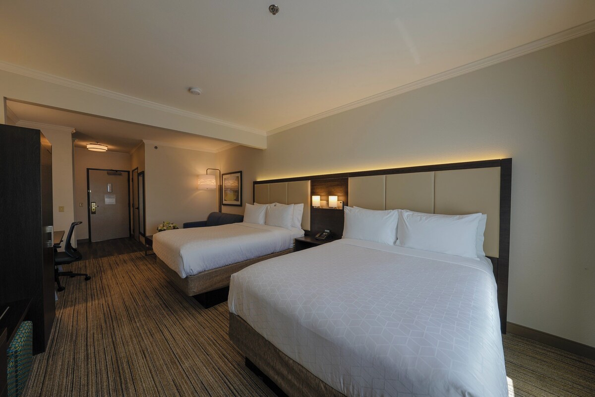 A hotel room with two beds, a desk, a chair, and a TV.