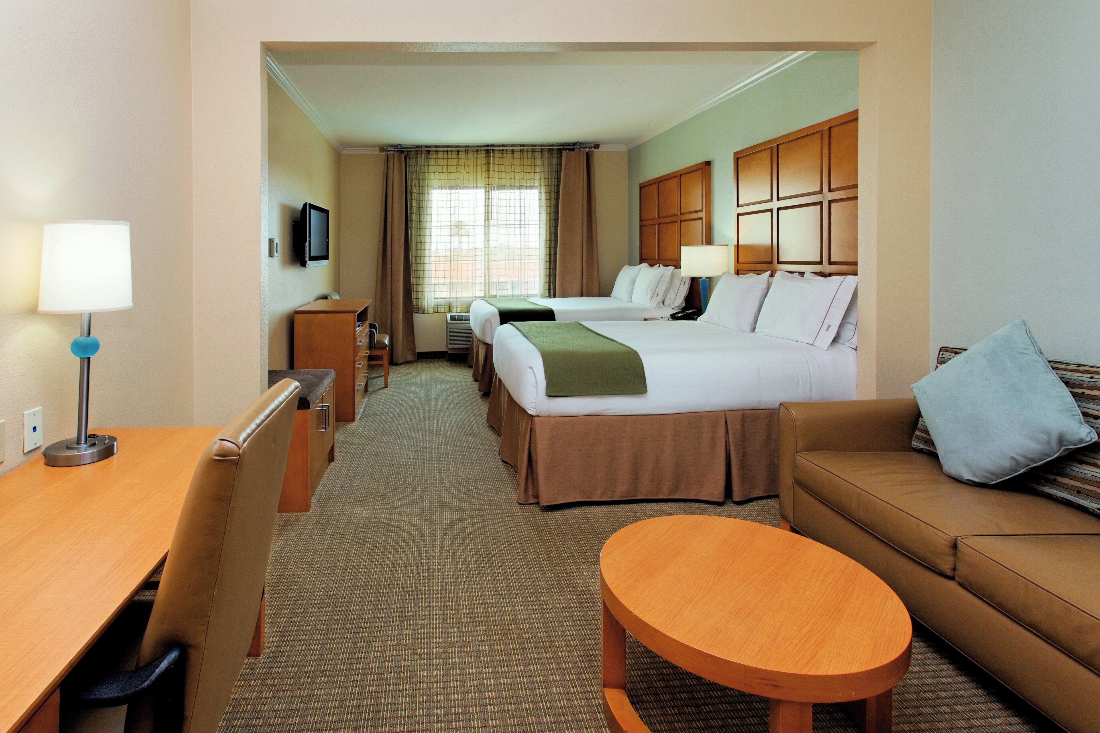 A hotel room with a bed, two bedside tables, a desk, a chair, a sofa, and a small round table.