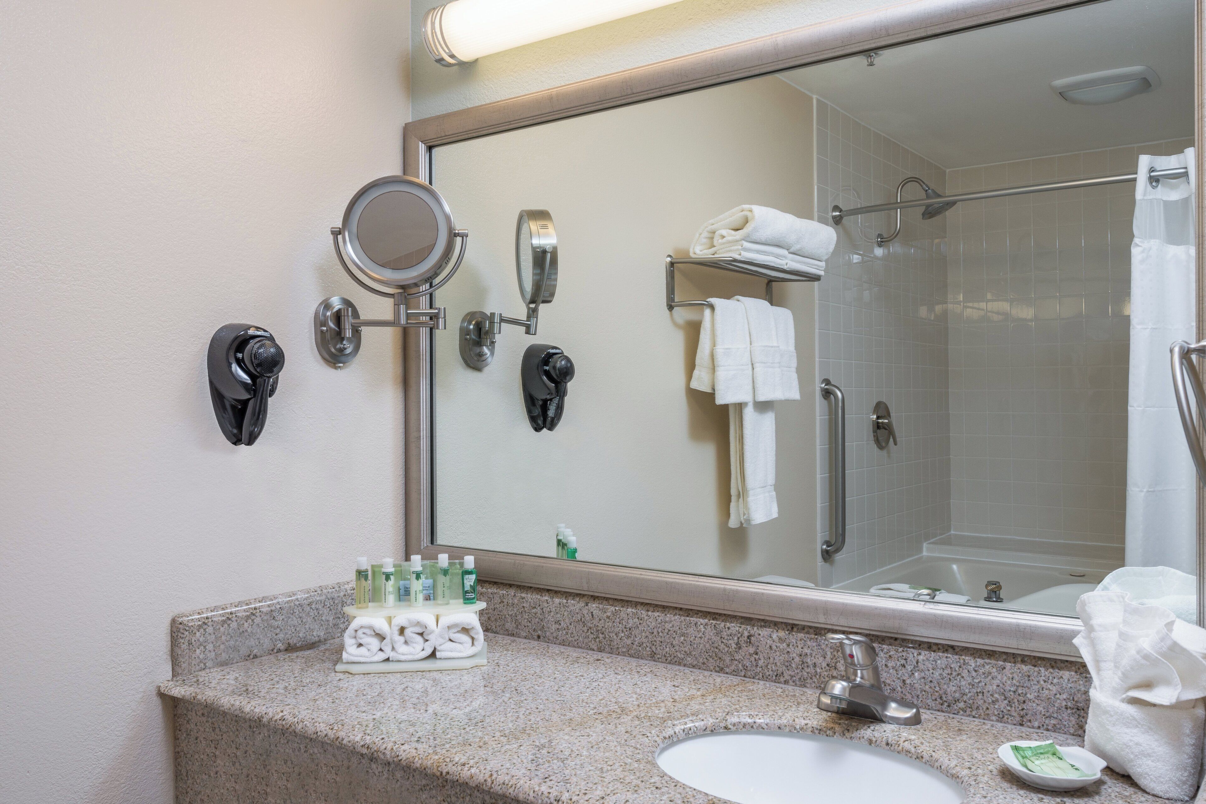 A bathroom with a large mirror, a sink, and a shower.