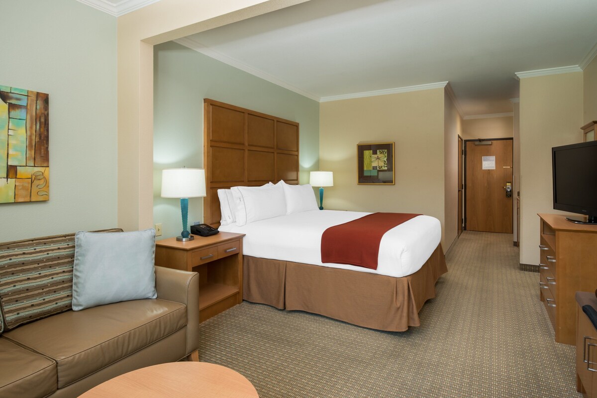 A hotel room with a large bed, a desk with a lamp, a television, and a sofa.