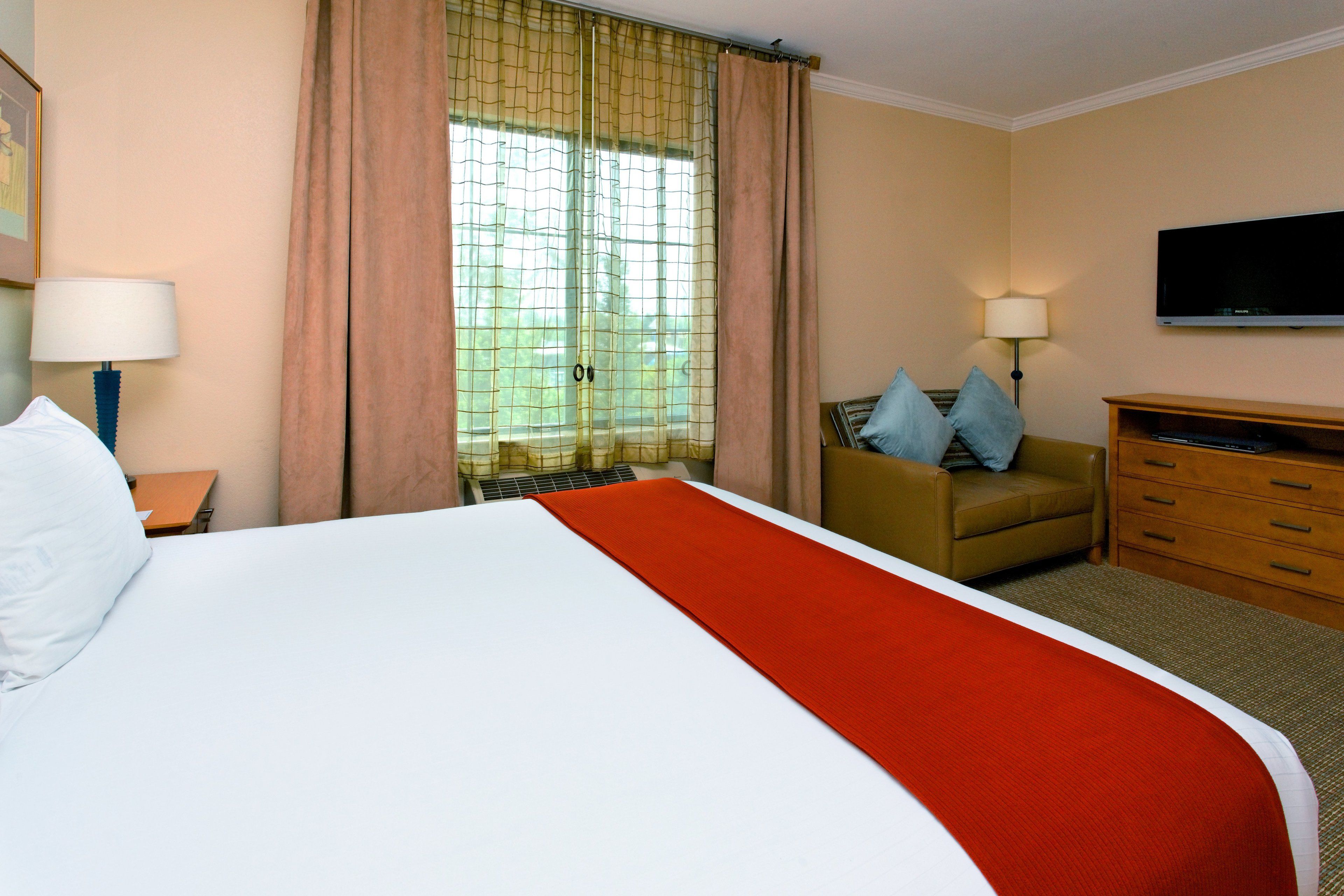 A hotel room with a large bed, a desk, a chair, a television, and a window with curtains.