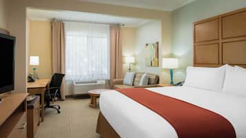 A hotel room with a bed, desk, chair, television, air conditioning unit, and a painting on the wall.