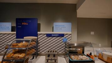 A bakery counter with various baked goods, a toaster, and a sign indicating breakfast is ready when you are.