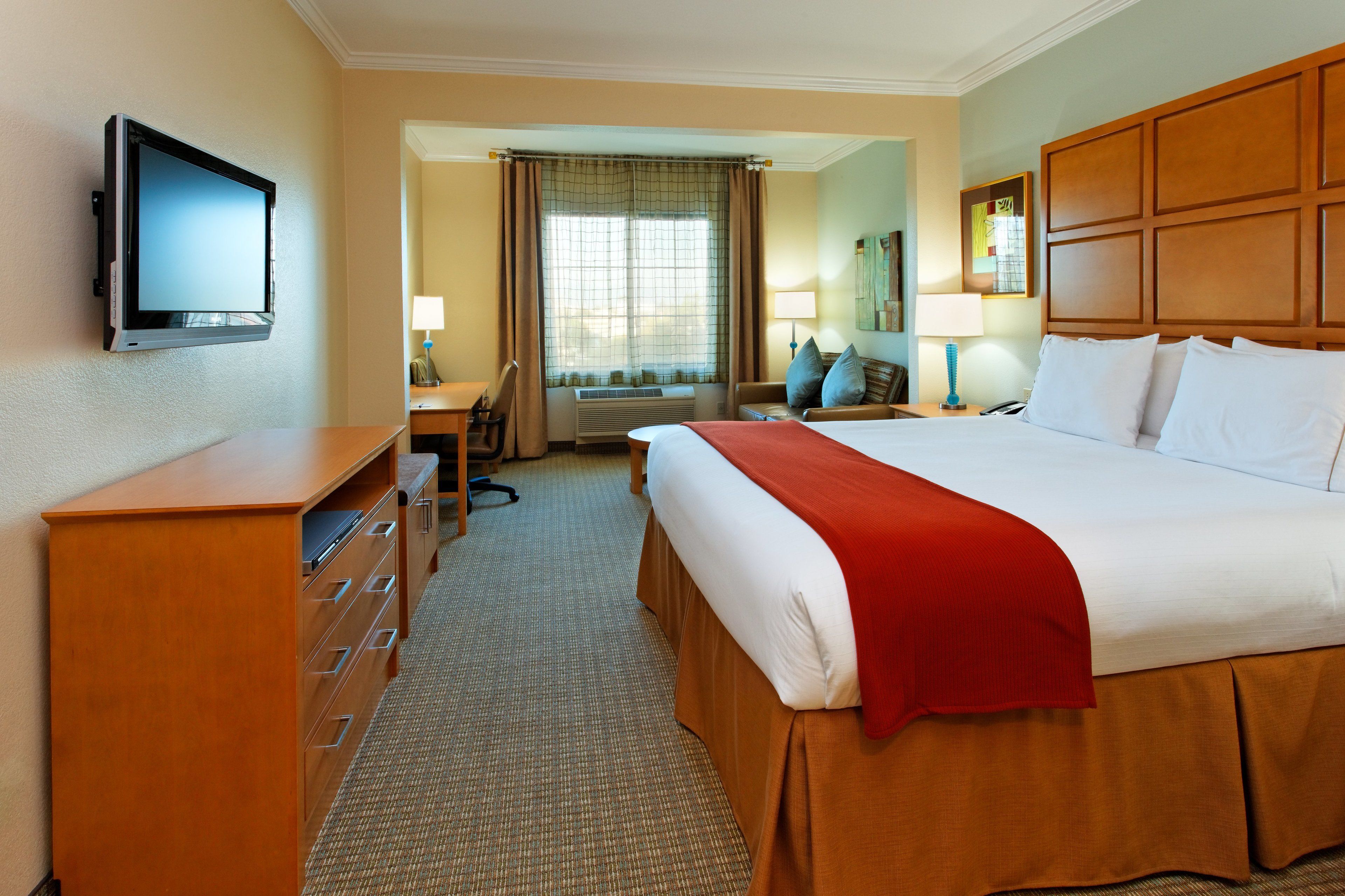 A hotel room with a bed, a desk, a chair, a TV, and a window with curtains.