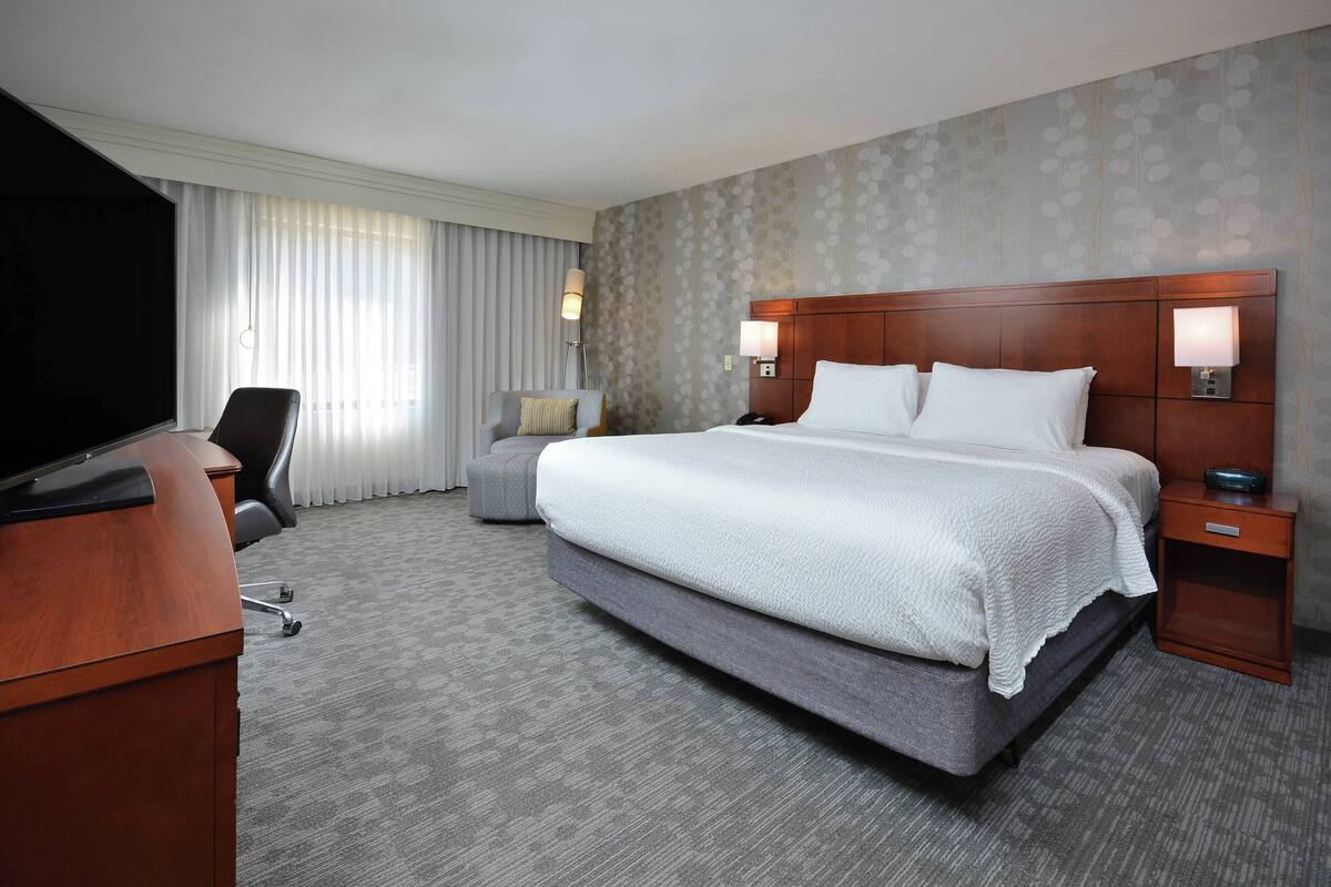 A hotel room with a large bed, a desk, a chair, and a TV.