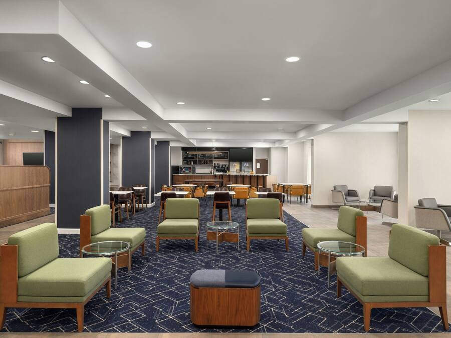 Un vestíbulo de hotel con una zona de estar central, un bar y un mostrador de recepción.