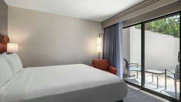A hotel room with a large bed, a desk, a chair, and a view of the outdoors.