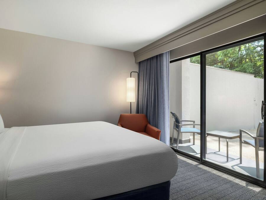 A hotel room with a large bed, a desk, a chair, and a view of the outdoors.