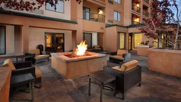 An outdoor seating area with a fire feature, wicker furniture, and a building with multiple balconies.