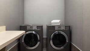 A laundry room with two front-loading LG washers and dryers, a white towel on the dryer, and a beige countertop. - Courtyard by Marriott Beckley (Beckley)