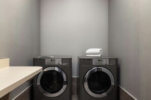 A laundry room with two front-loading LG washers and dryers, a white towel on the dryer, and a beige countertop. - Courtyard by Marriott Beckley (Beckley)