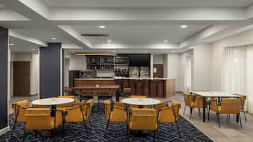 A modern hotel room with a bar area, multiple seating arrangements, and a large television screen.