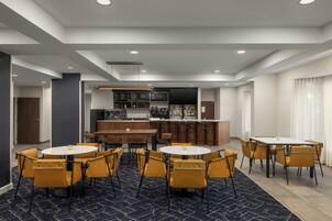 Una habitación de hotel moderna con una zona de bar, varios arreglos de asientos y una pantalla de televisión grande.