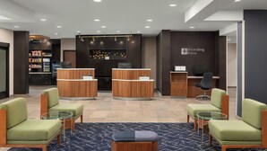 A modern hotel lobby with two reception desks, a seating area with green upholstered chairs, a bar area, and a 'Boarding Pass' sign. - Courtyard by Marriott Beckley (Beckley)