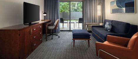 A hotel room with a flat-screen TV, a desk with a chair, a sofa, a small table, and a painting on the wall.