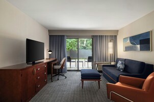 Habitación de hotel con televisor de pantalla plana, escritorio con silla, sofá, mesita pequeña y un cuadro en la pared.