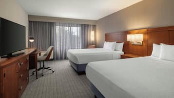 A hotel room with two beds, a desk with a TV, a chair, and a large window with curtains.