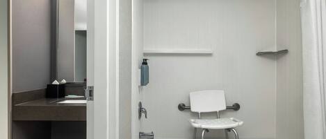 A bathroom with a bathtub, a shower, a toilet with a safety bar, and a towel rack.