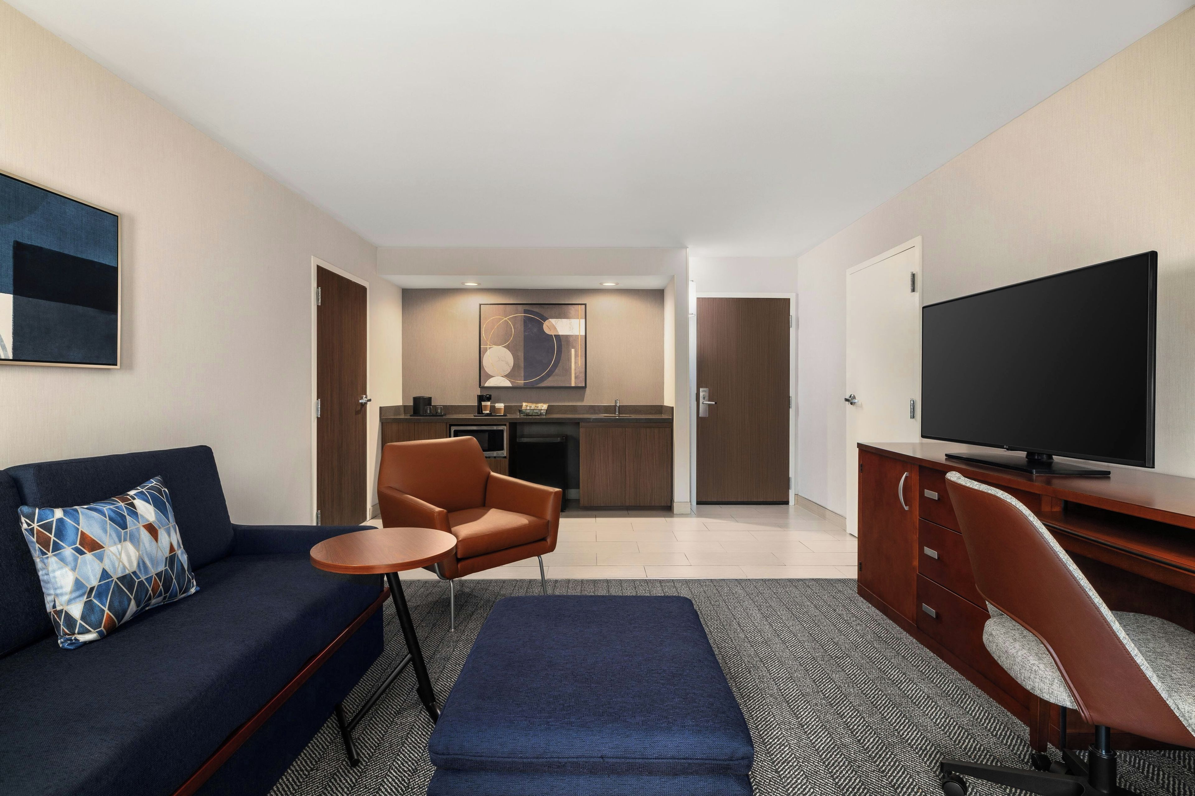 Een moderne hotelkamer met een bank, een tafeltje, een televisie en een kitchenette.