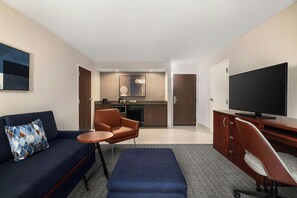 A modern hotel room with a sofa, a small table, a TV, and a kitchenette. - Courtyard by Marriott Beckley (Beckley)