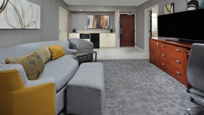 A modern hotel room with a grey sofa, a small table, a television, a wooden cabinet, and a kitchenette in the background. - Courtyard by Marriott Beckley (Beckley)