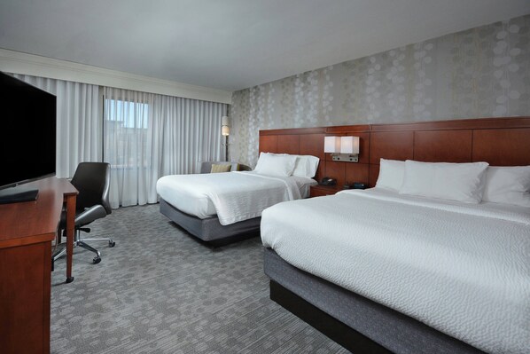 A hotel room with two beds, a desk, a TV, and a large window with curtains. - Courtyard by Marriott Beckley (Beckley)