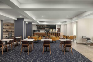 A modern hotel dining area with multiple tables and chairs, a bar, and a kitchen in the background. - Courtyard by Marriott Beckley (Beckley)
