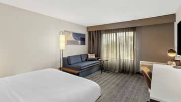 A hotel room with a large bed, a sofa, a small table, and a desk.