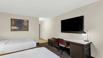 Habitación de hotel con dos camas, un escritorio, una silla, un televisor y una obra de arte colgada en la pared.