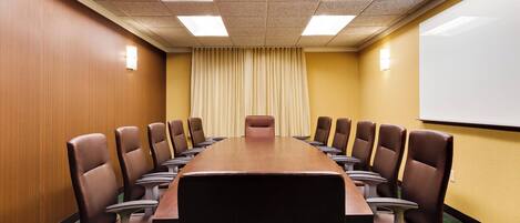 A conference room with a long table and chairs, a projector screen, and a window with curtains.