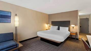 A hotel room with a large bed, a desk, a chair, a sofa, and a wall-mounted TV.