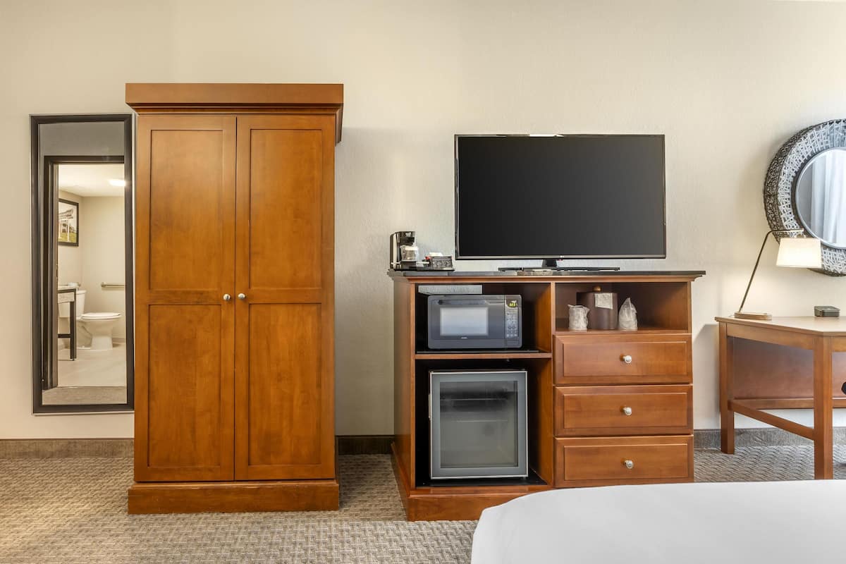 A hotel room with a wooden wardrobe, a television, a microwave, a refrigerator, and a desk with a lamp.