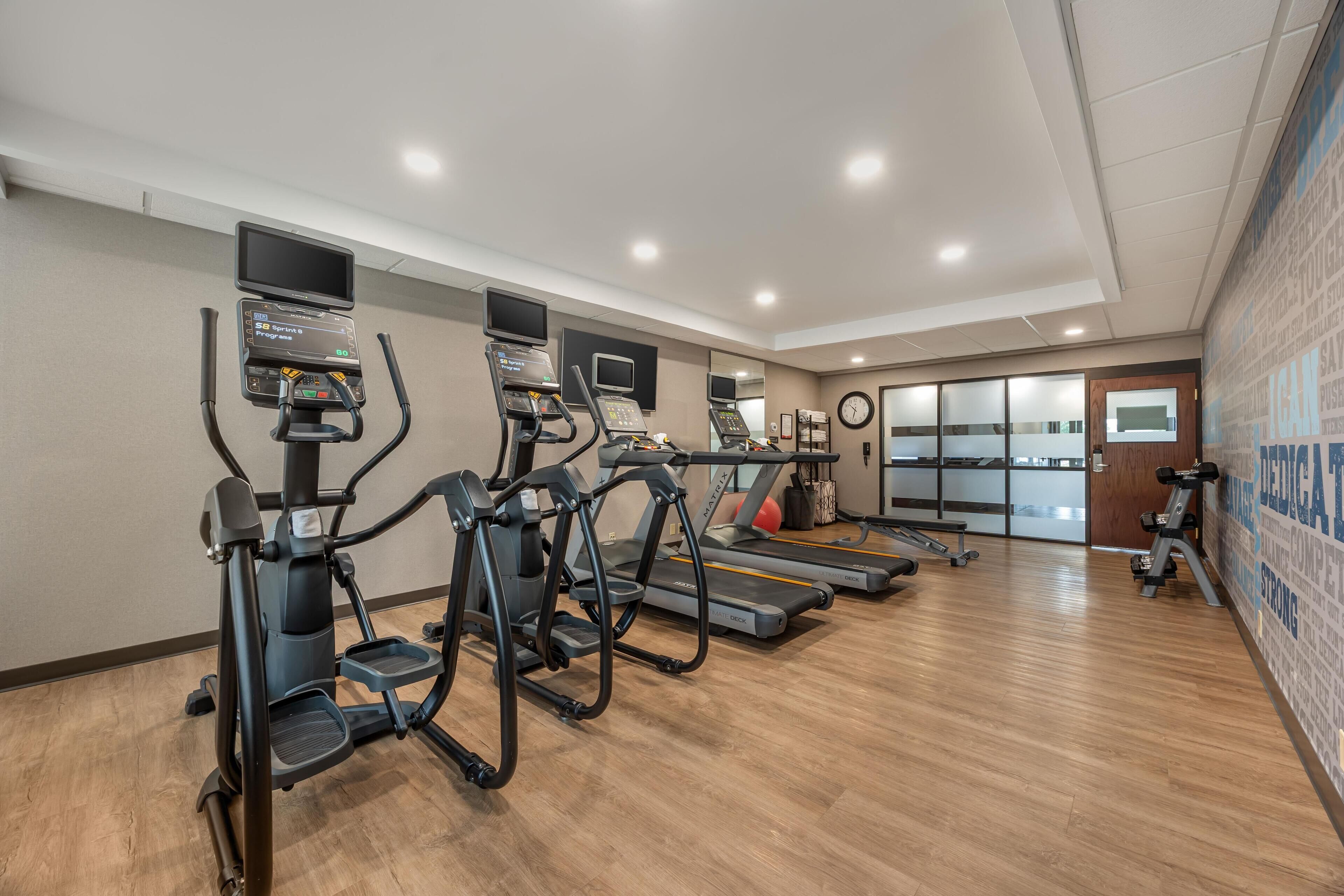 Ein Fitnessstudio mit Laufbändern, Crosstrainern und einer Wand mit motivierenden Sprüchen.