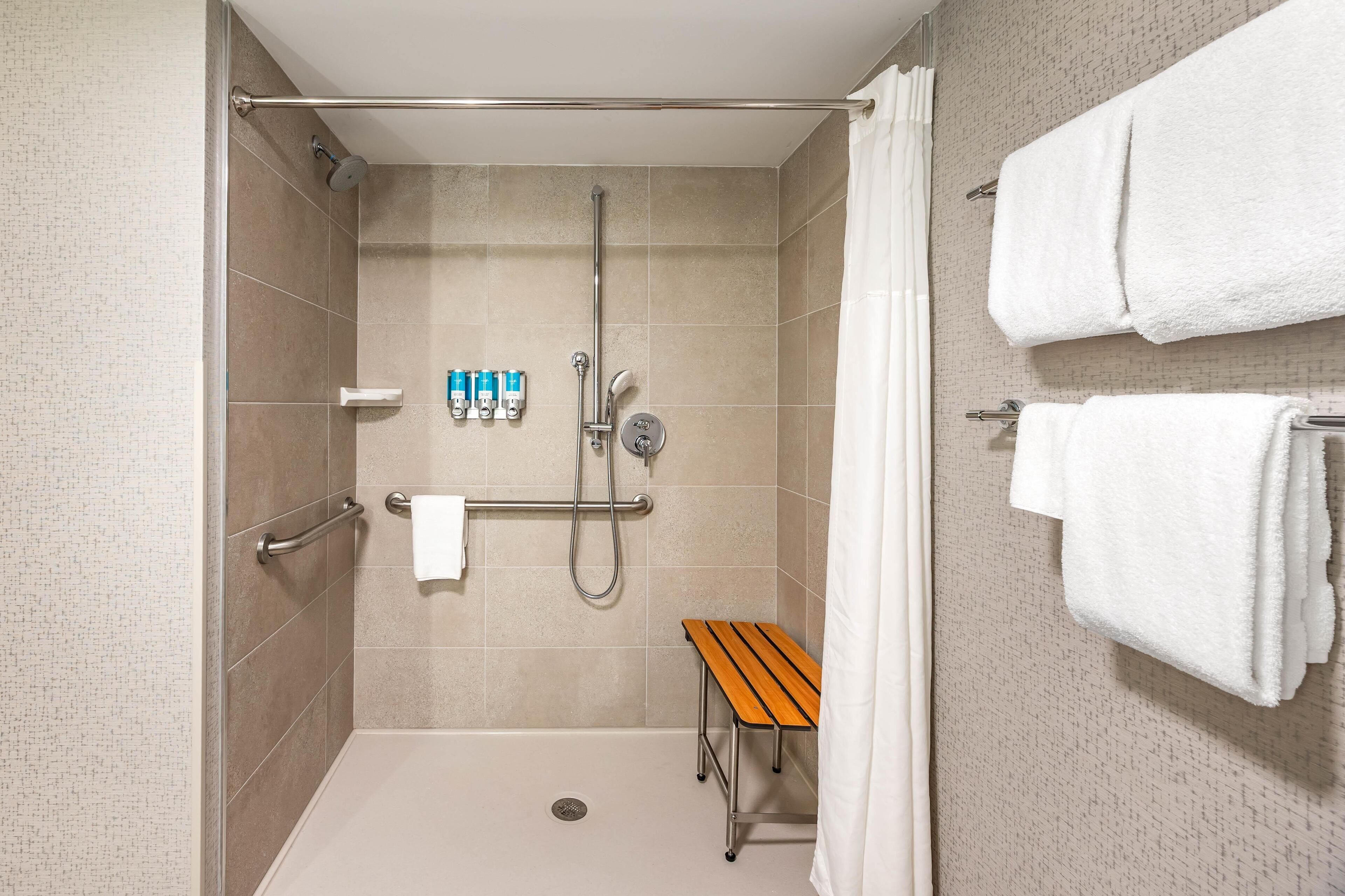 A shower area with a bench, handrails, and a towel rack.