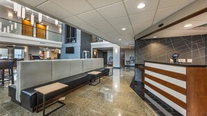 Eine moderne Lobby mit Empfangsschalter, einer Sitzecke und einer hohen Decke mit eingelassener Beleuchtung.