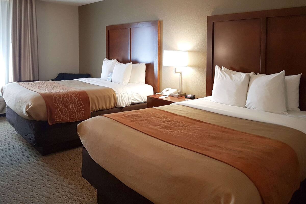 Habitación de hotel con dos camas, cada una con cabecero de madera, una mesita de noche con lámpara y teléfono.