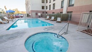 Une piscine avec un jacuzzi, entourée de chaises longues et délimitée par une clôture.
