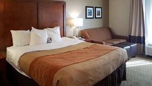 Une chambre d’hôtel avec un grand lit, un canapé, une table de chevet avec une lampe et des tableaux encadrés au mur.