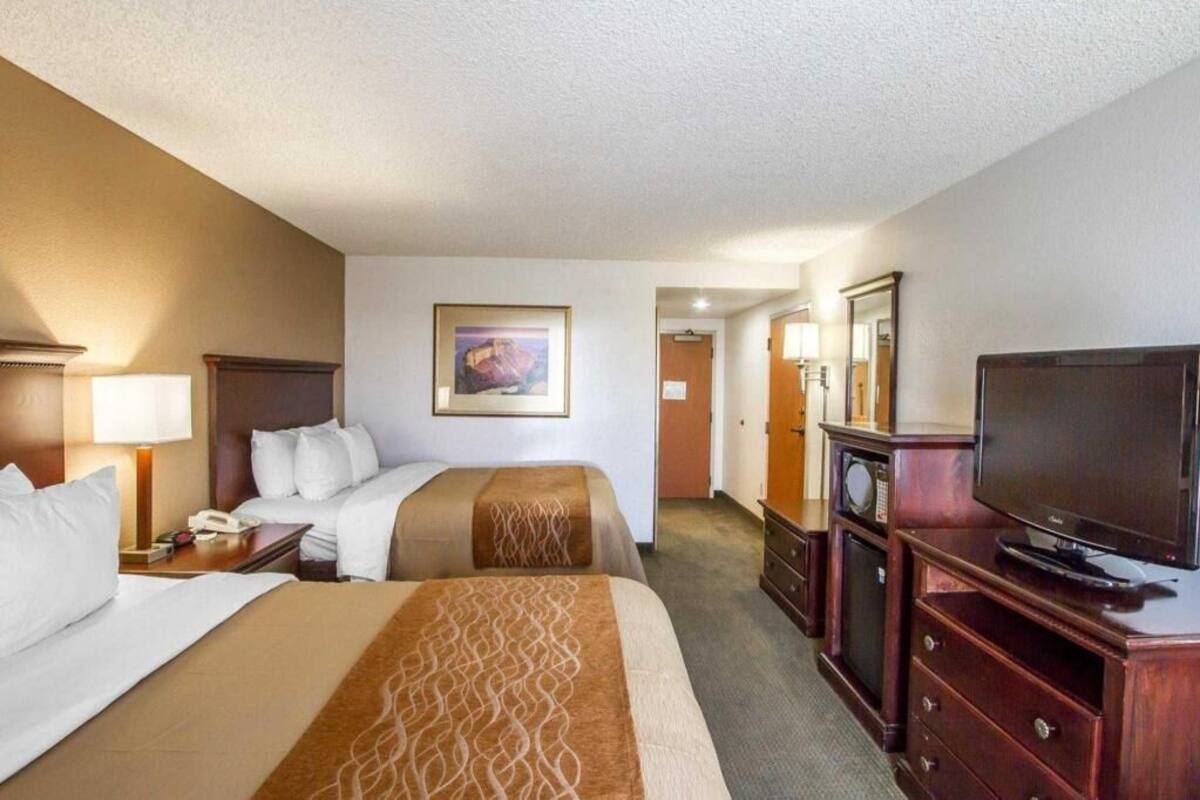 Una habitación de hotel con dos camas, una televisión, un escritorio con lámpara y un cuadro en la pared.