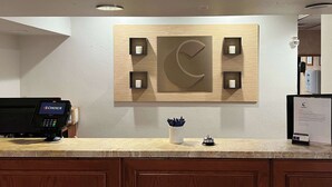 Un espace d’accueil d’hôtel avec un panneau en bois fixé au mur, une caisse enregistreuse et un petit bureau sur lequel se trouve un pot à crayons.