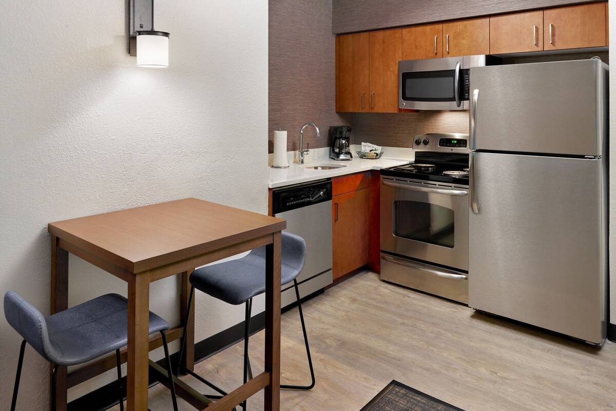 Una cocina compacta con armarios de madera, un refrigerador de acero inoxidable, un microondas, una cafetera y un lavavajillas.