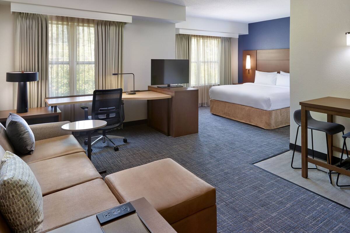 Una habitación de hotel con cama, escritorio con silla, sofá y televisión.