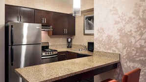 A kitchen with dark wooden cabinets, stainless steel appliances, a granite countertop, and a red chair.