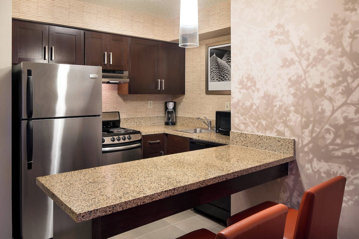 A kitchen with dark wooden cabinets, stainless steel appliances, a granite countertop, and a red chair.