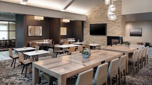 A spacious conference room with multiple tables and chairs, a stone accent wall, a flat-screen TV, and a fireplace.
