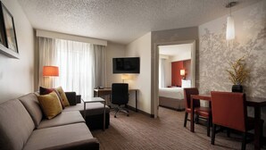 A hotel room with a sofa, a desk, a chair, a TV, and a bed.