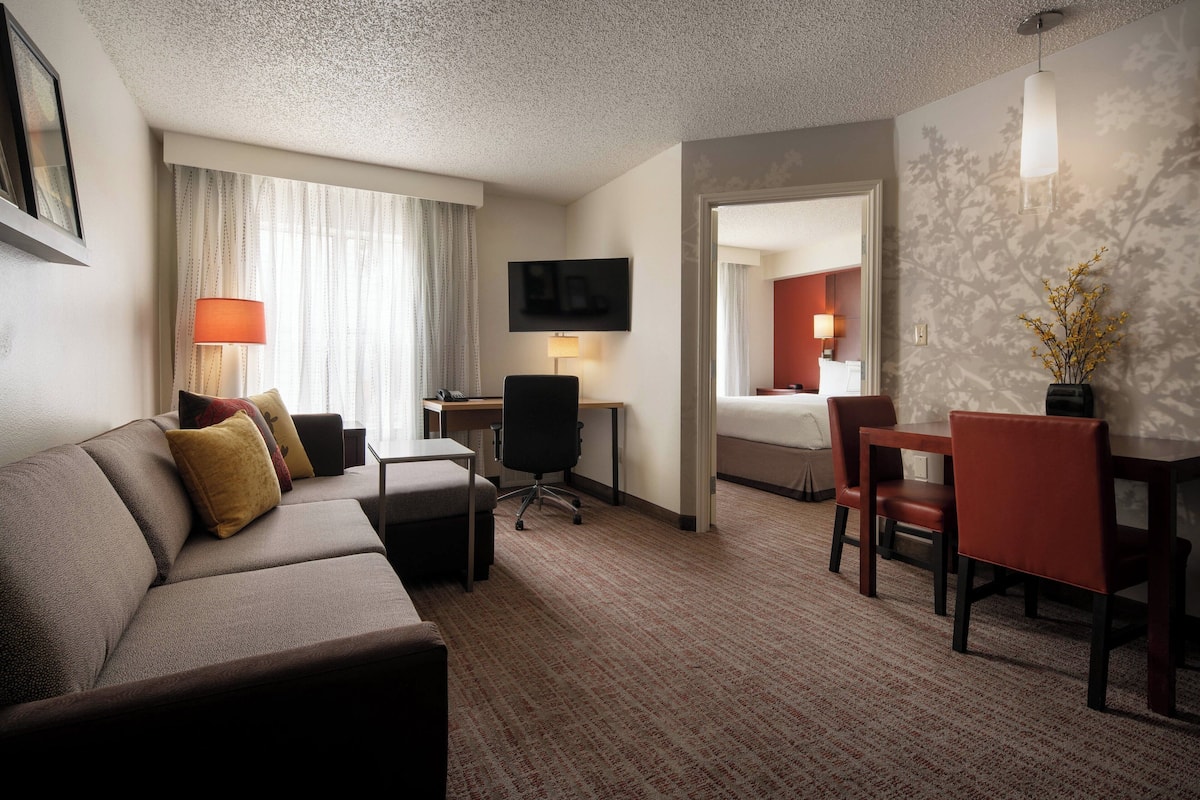 A hotel room with a sofa, a desk, a chair, a TV, and a bed.